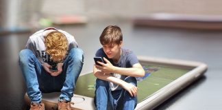 dos adolescentes usando sus dispositivos móviles. De fondo un smartphone